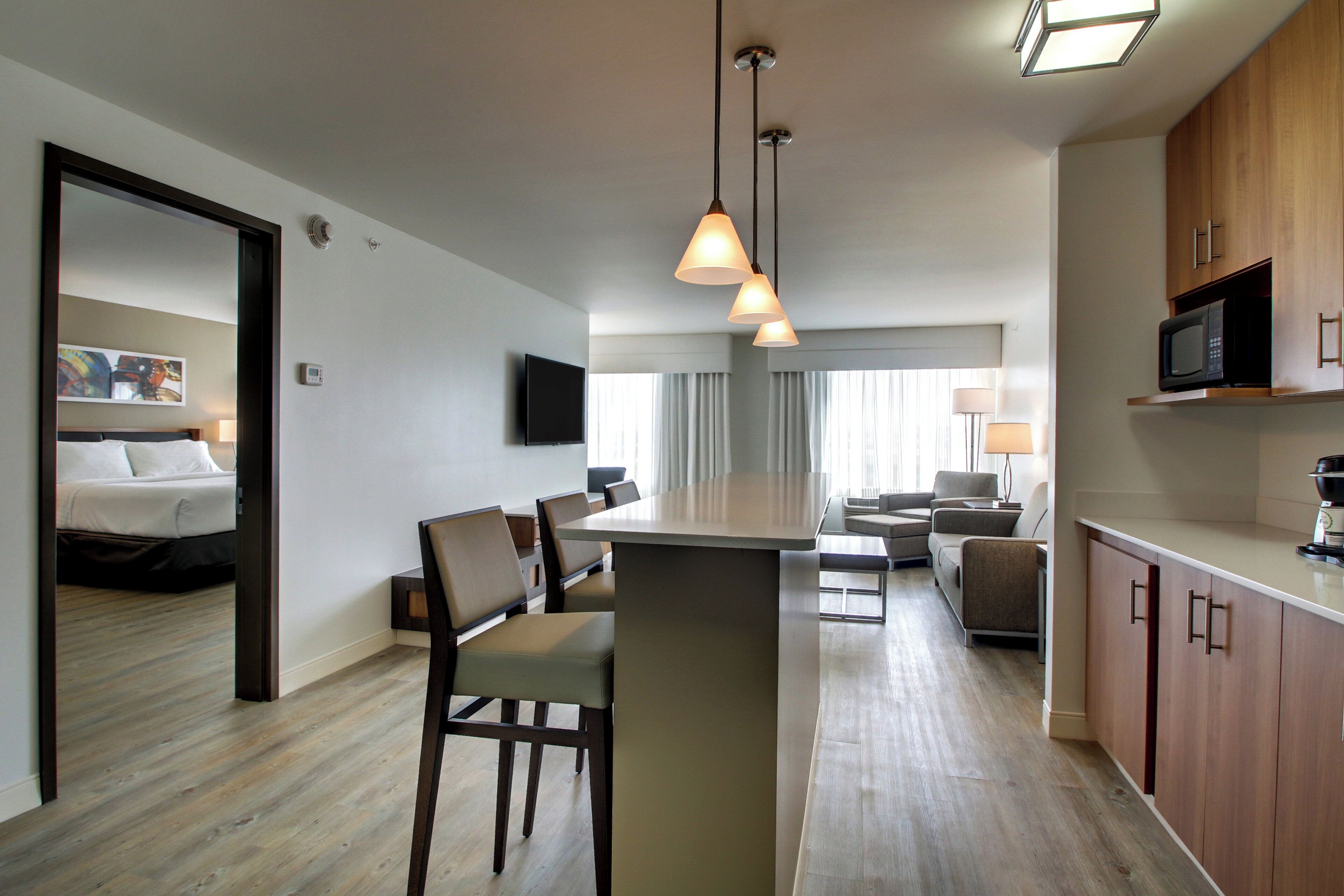 A modern hotel room with a dining area, kitchenette, and a TV mounted on the wall.