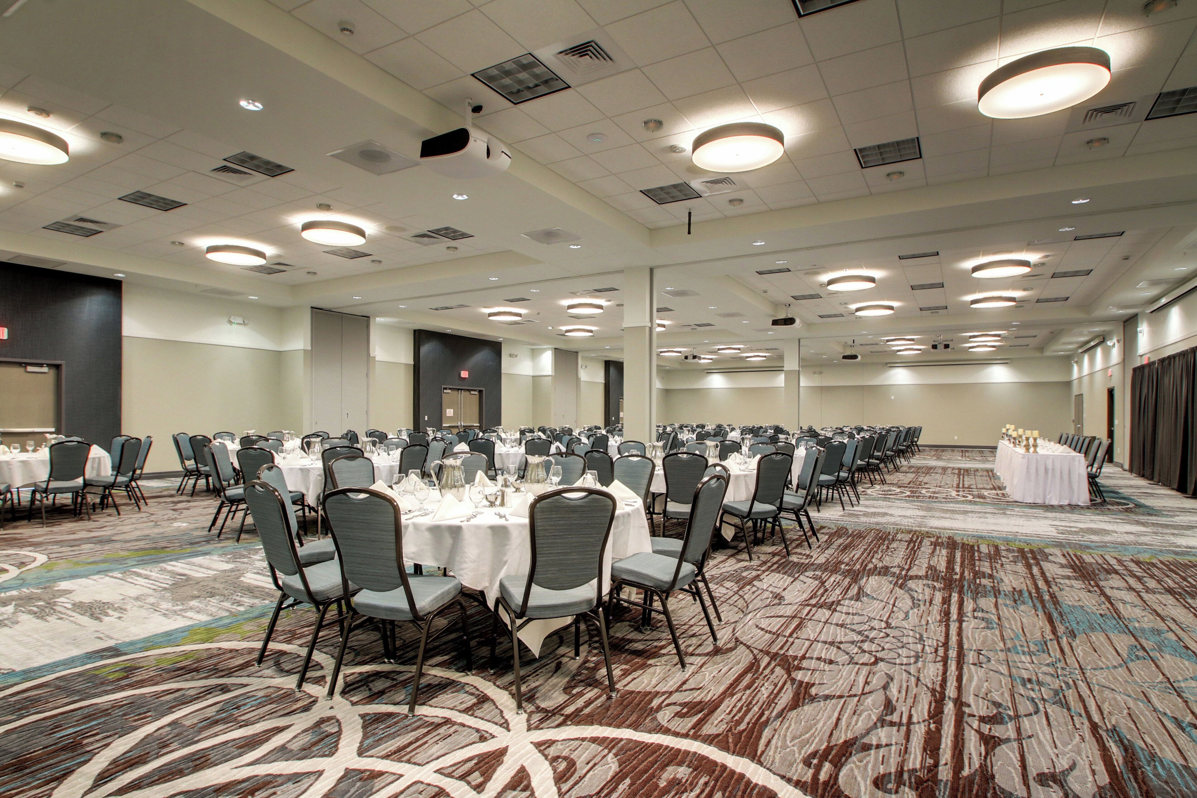 A large conference room with multiple round tables, chairs, and a carpeted floor.