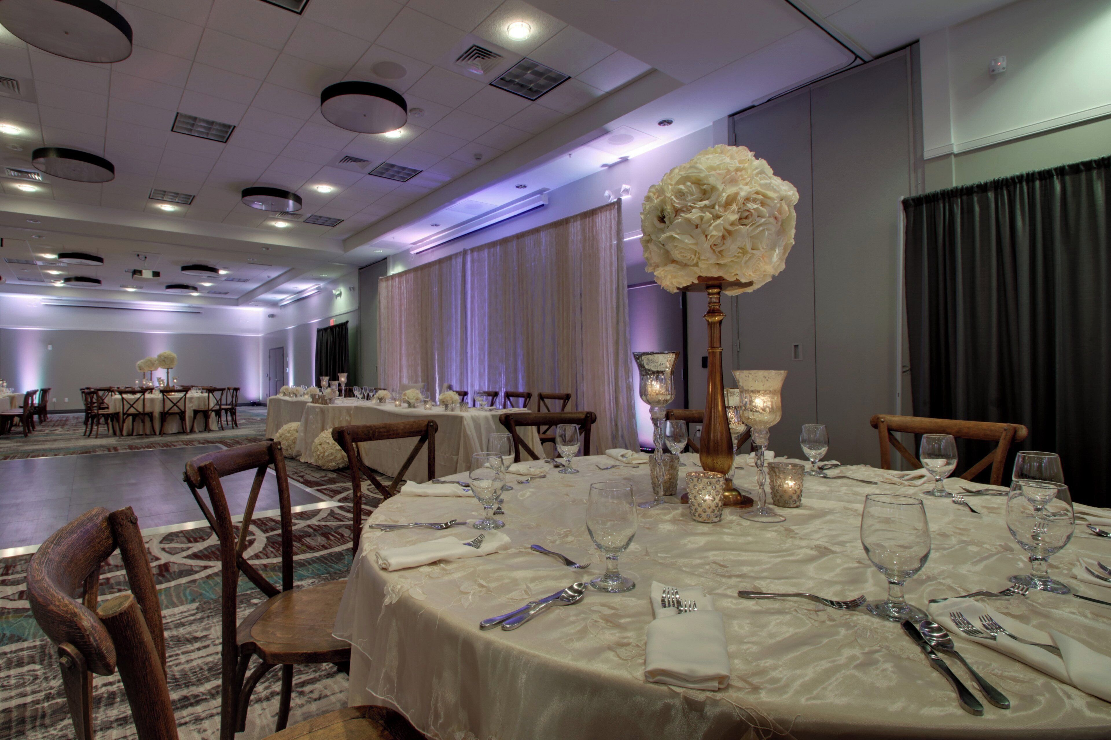 Une salle de banquet avec des tables rondes dressées pour le repas, agrémentées de nappes blanches, de couverts en argent et de verres.