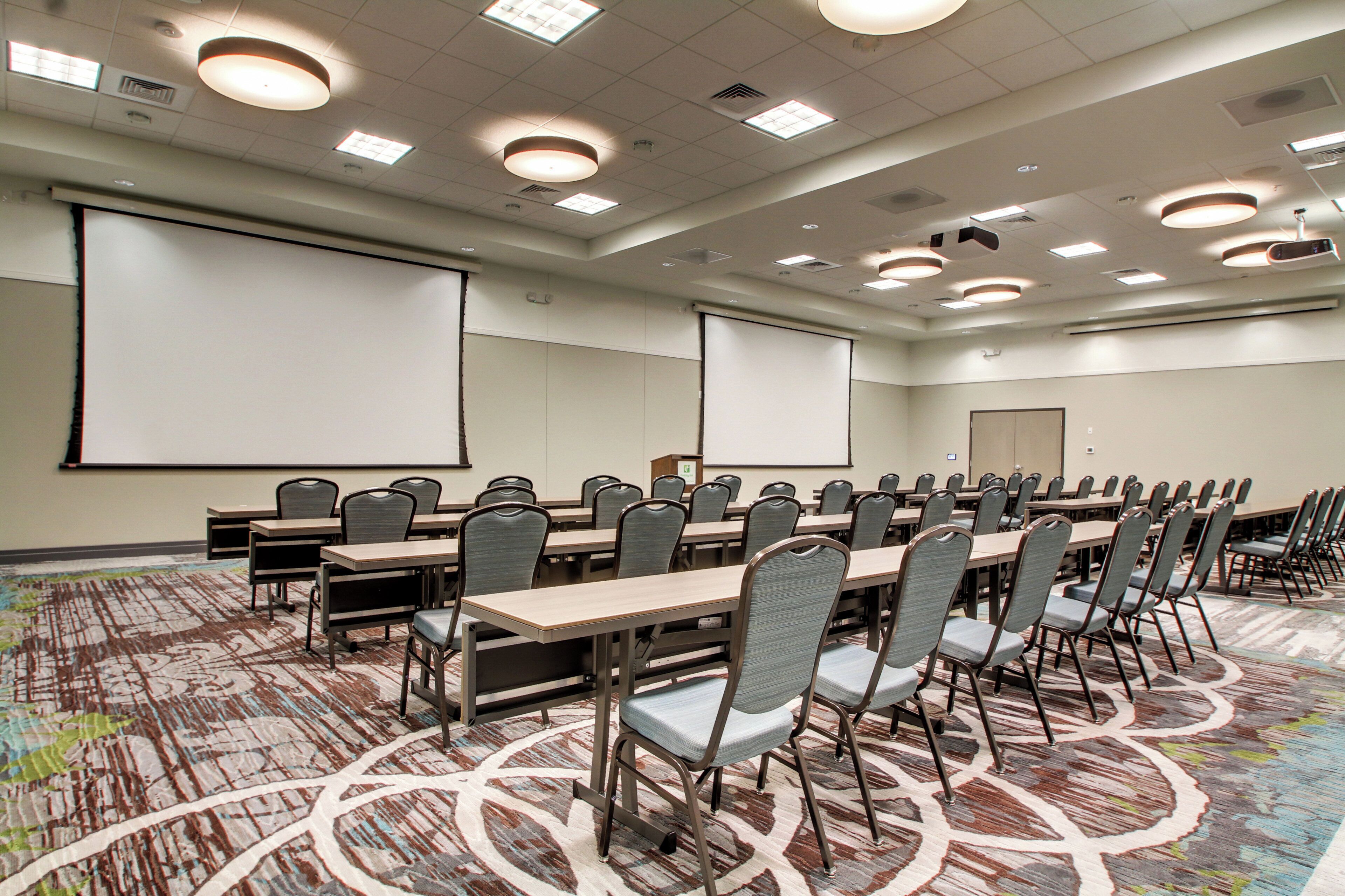 A conference room with a large projection screen, multiple tables, and chairs.