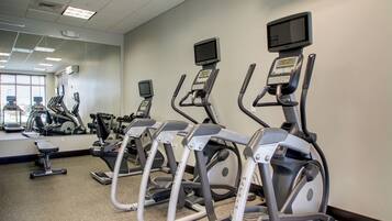 Une salle de sport équipée de tapis de course, de vélos d’appartement et d’un mur recouvert de miroirs.