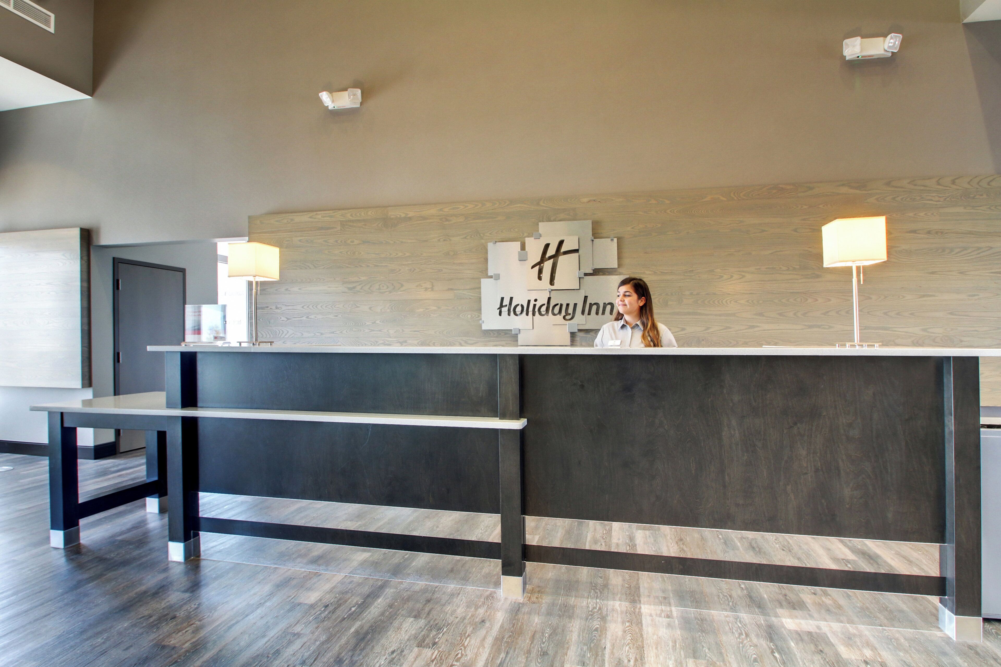 A reception desk at Holiday Inn with a modern design, a wooden wall backdrop, and a sign indicating the hotel name.