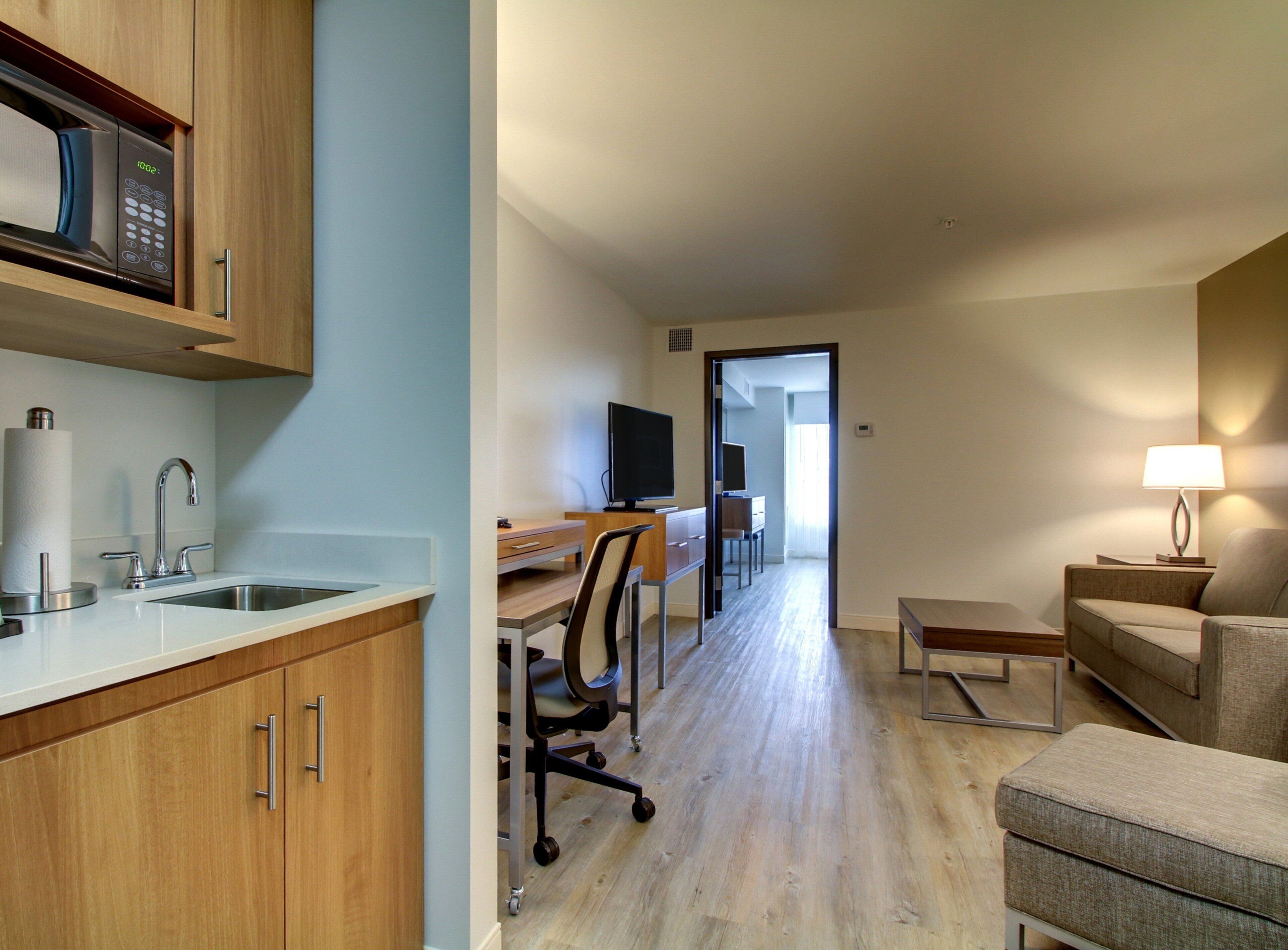 A modern kitchen with a microwave, sink, and cabinets. There is a dining area with a table and chairs, and a living area with a sofa and a lamp.