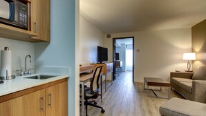 A modern kitchen with a microwave, sink, and cabinets. There is a dining area with a table and chairs, and a living room with a sofa and a lamp. - Holiday Inn & Suites Peoria At Grand Prairie by IHG (Peoria)