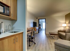 A modern kitchen with a microwave, sink, and cabinets. There is a dining area with a table and chairs, and a living room with a sofa and a lamp. - Holiday Inn & Suites Peoria At Grand Prairie by IHG (Peoria)
