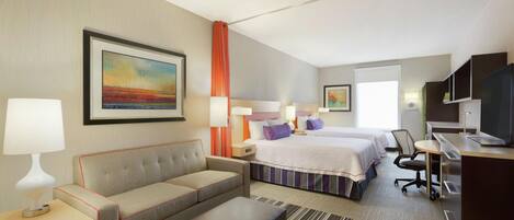 A hotel room with a sofa, a desk, a bed, and a television.