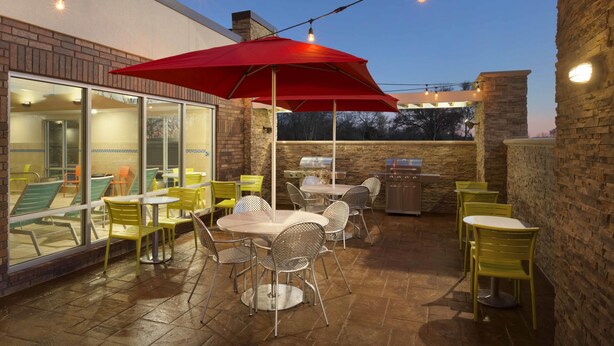 An outdoor patio with tables and chairs, a red umbrella, and string lights. - Home2 Suites by Hilton Fort Smith AR (Fort Smith)