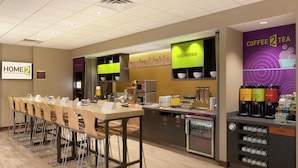 A hotel dining area with a long counter, chairs, a coffee station, and a trash bin. - Home2 Suites by Hilton Fort Smith AR (Fort Smith)
