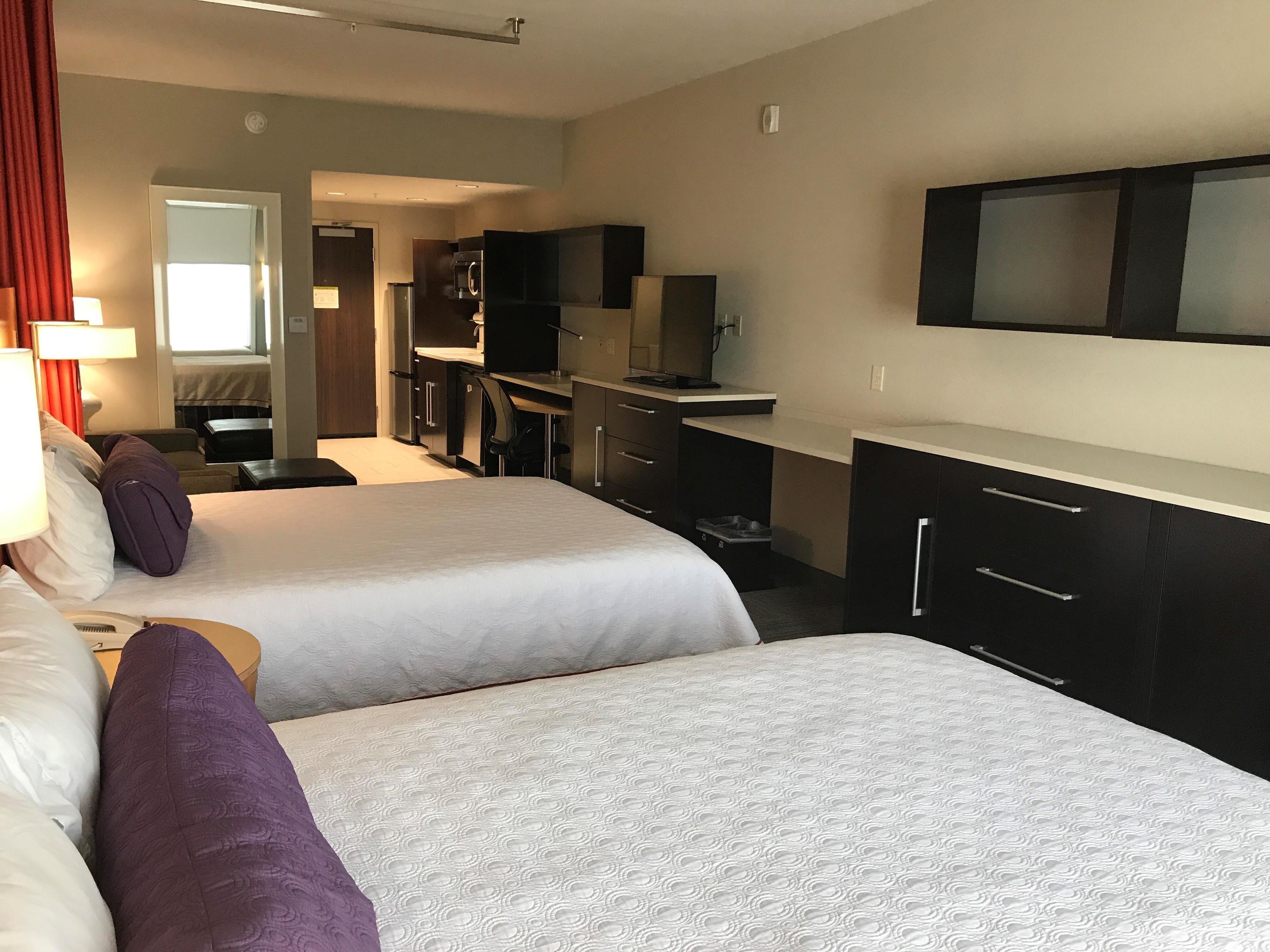 Habitación de hotel con dos camas, un escritorio, un televisor y una kitchenette.
