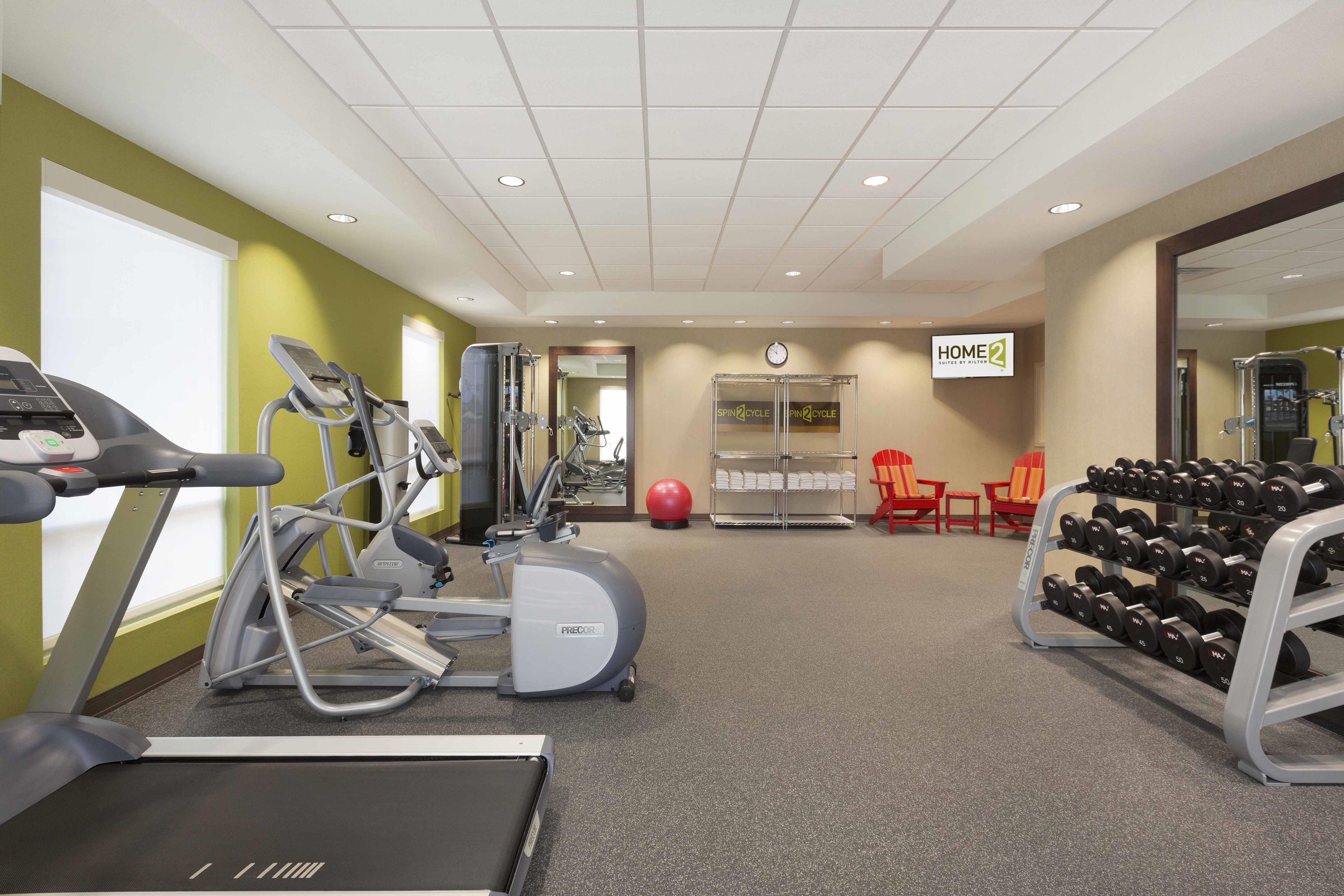 Un gimnasio con equipo de cardio, estaciones de levantamiento de pesas y un espejo grande.