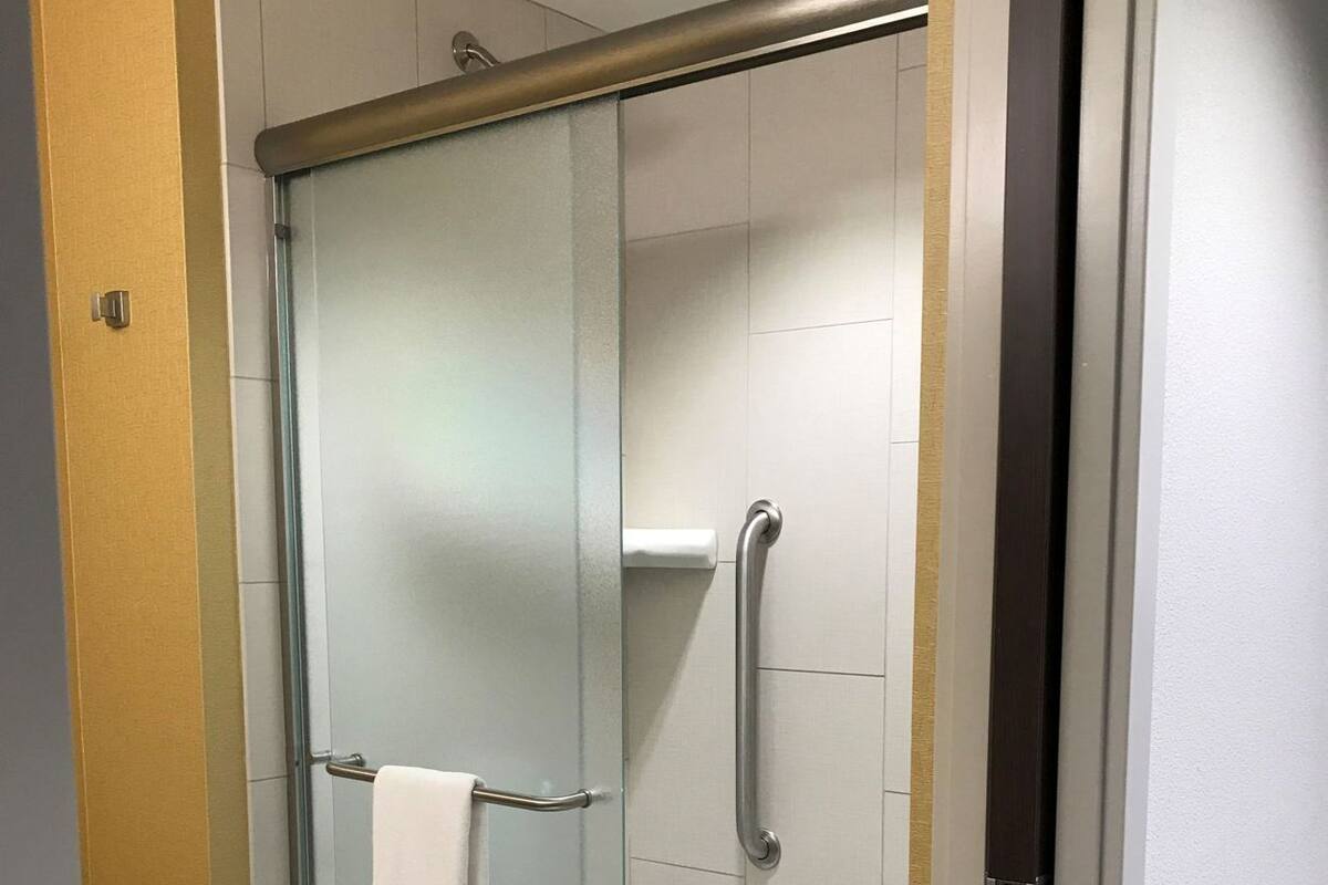 A glass-enclosed shower stall with a white towel hanging on a metal bar, a white toilet, and a white bathtub.