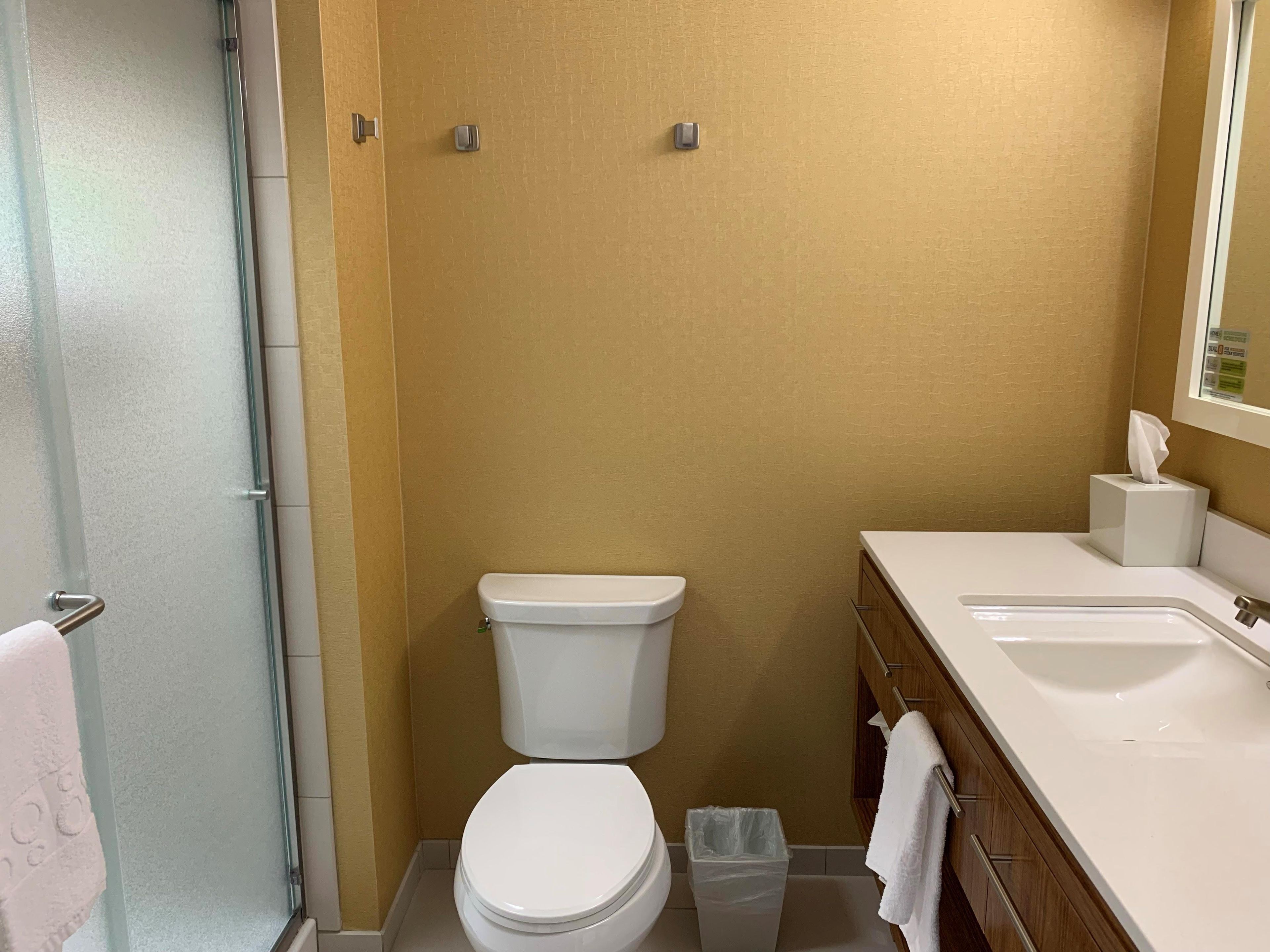 Un baño con inodoro, cubo de basura, lavamanos y toallero.
