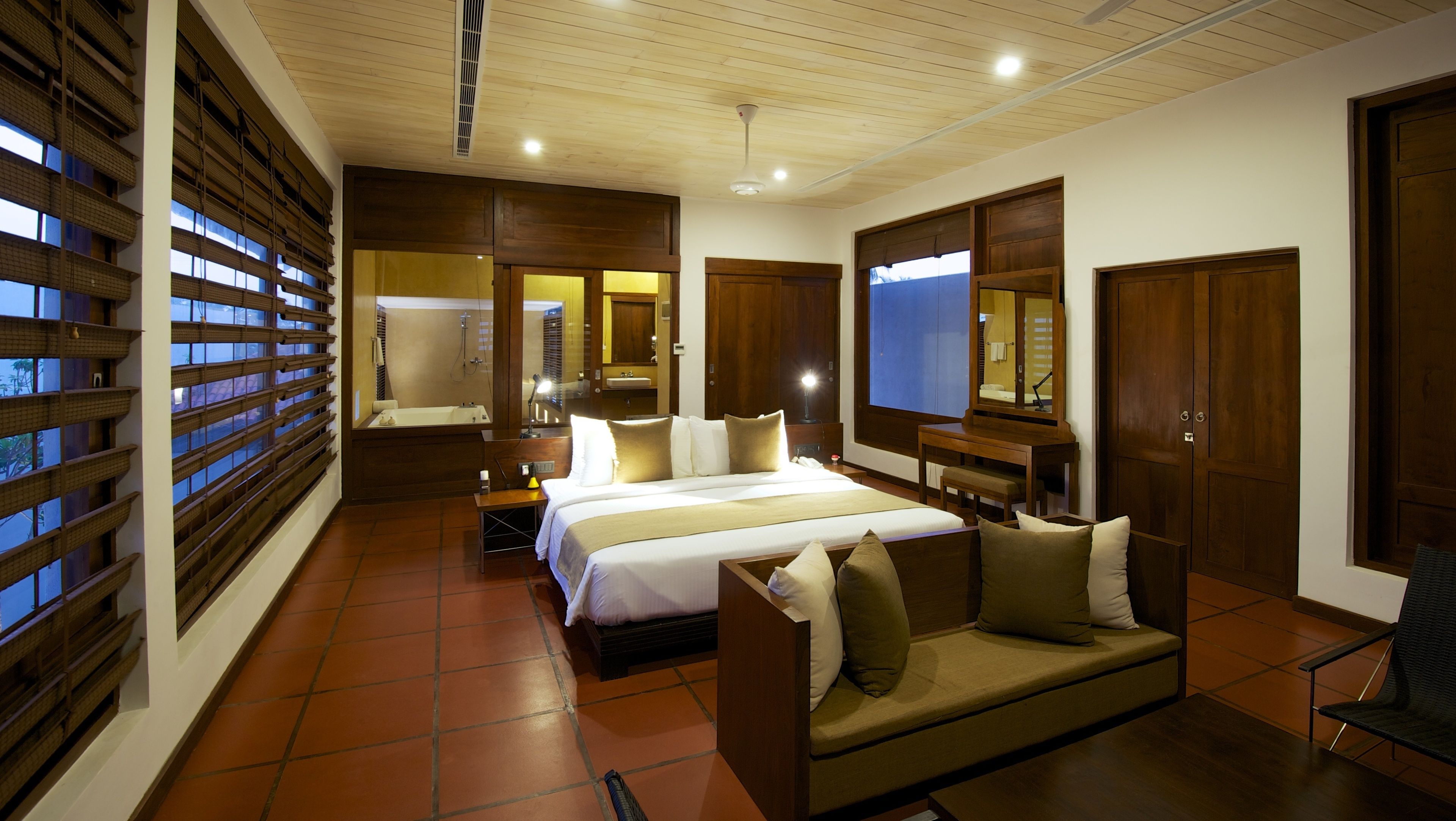 A hotel room with a large bed, a sofa, a desk, and a bathroom with a bathtub and shower.