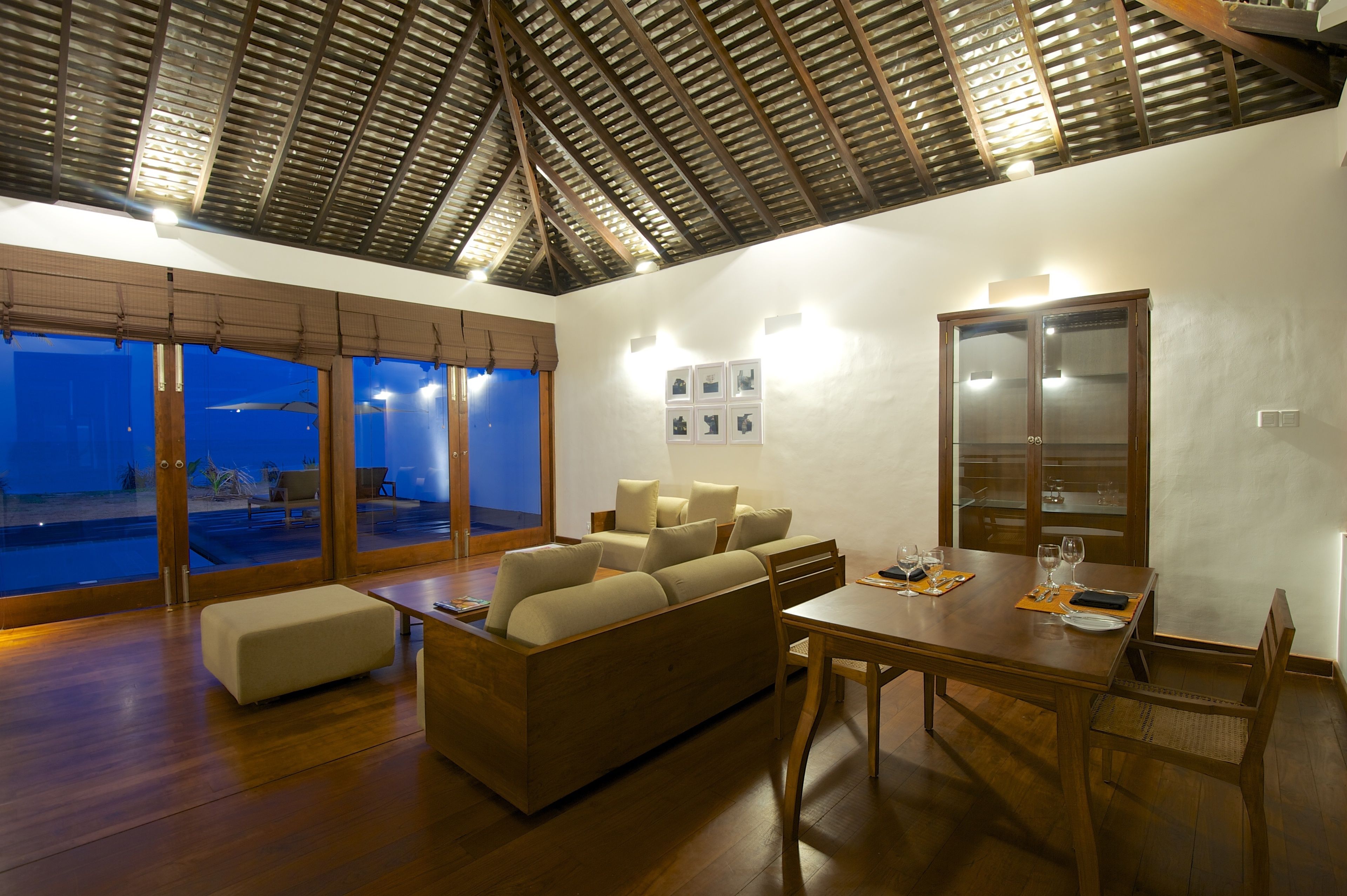 A modern interior with a wooden ceiling, a sofa, a dining table, and a view of a swimming pool.