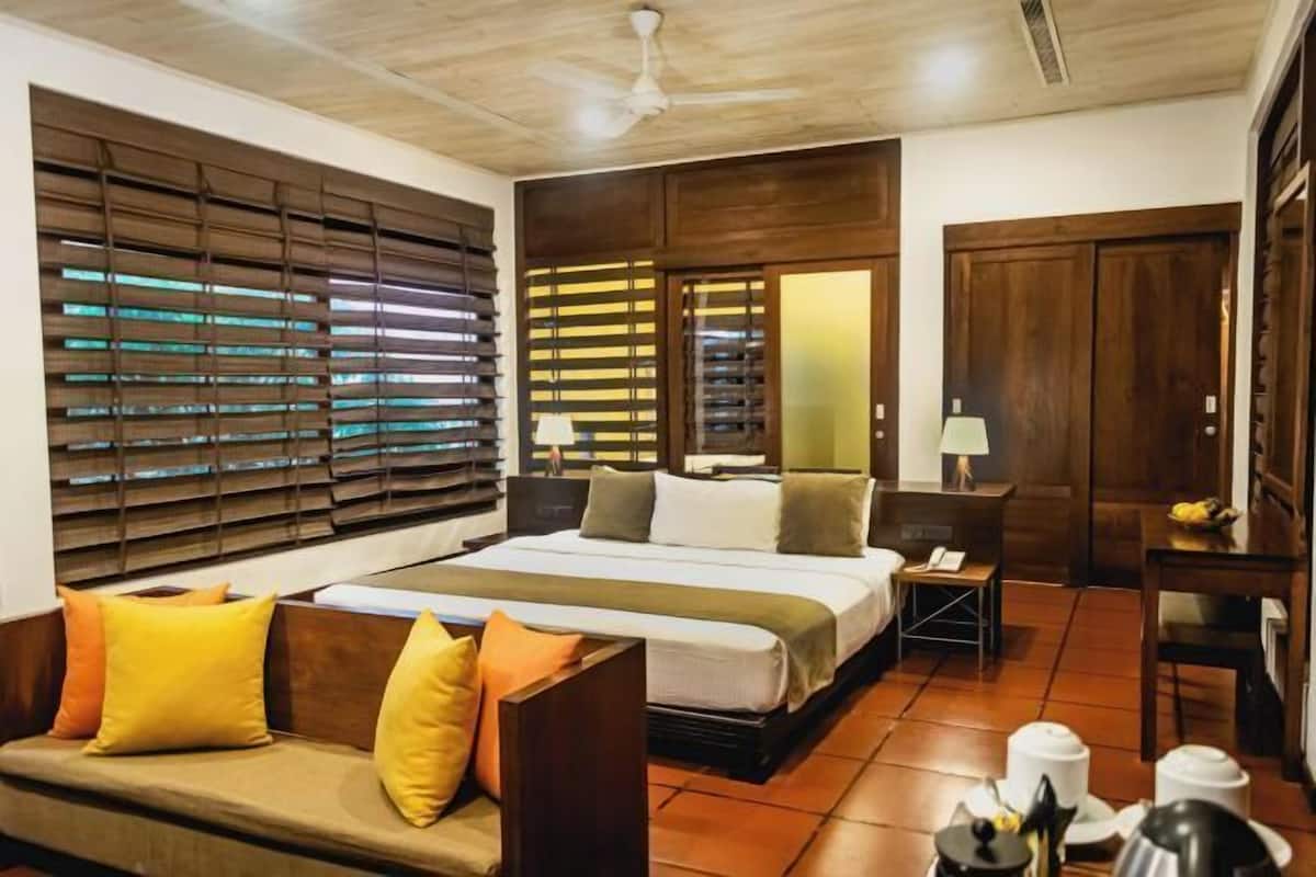 A hotel room with a bed, a sofa, a desk, and a window with blinds.