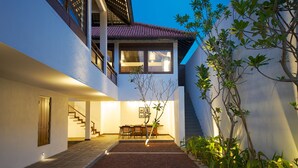 Una casa moderna con una escalera que conduce a un nivel superior, un comedor con mesa y sillas, y un pequeño jardín con plantas.