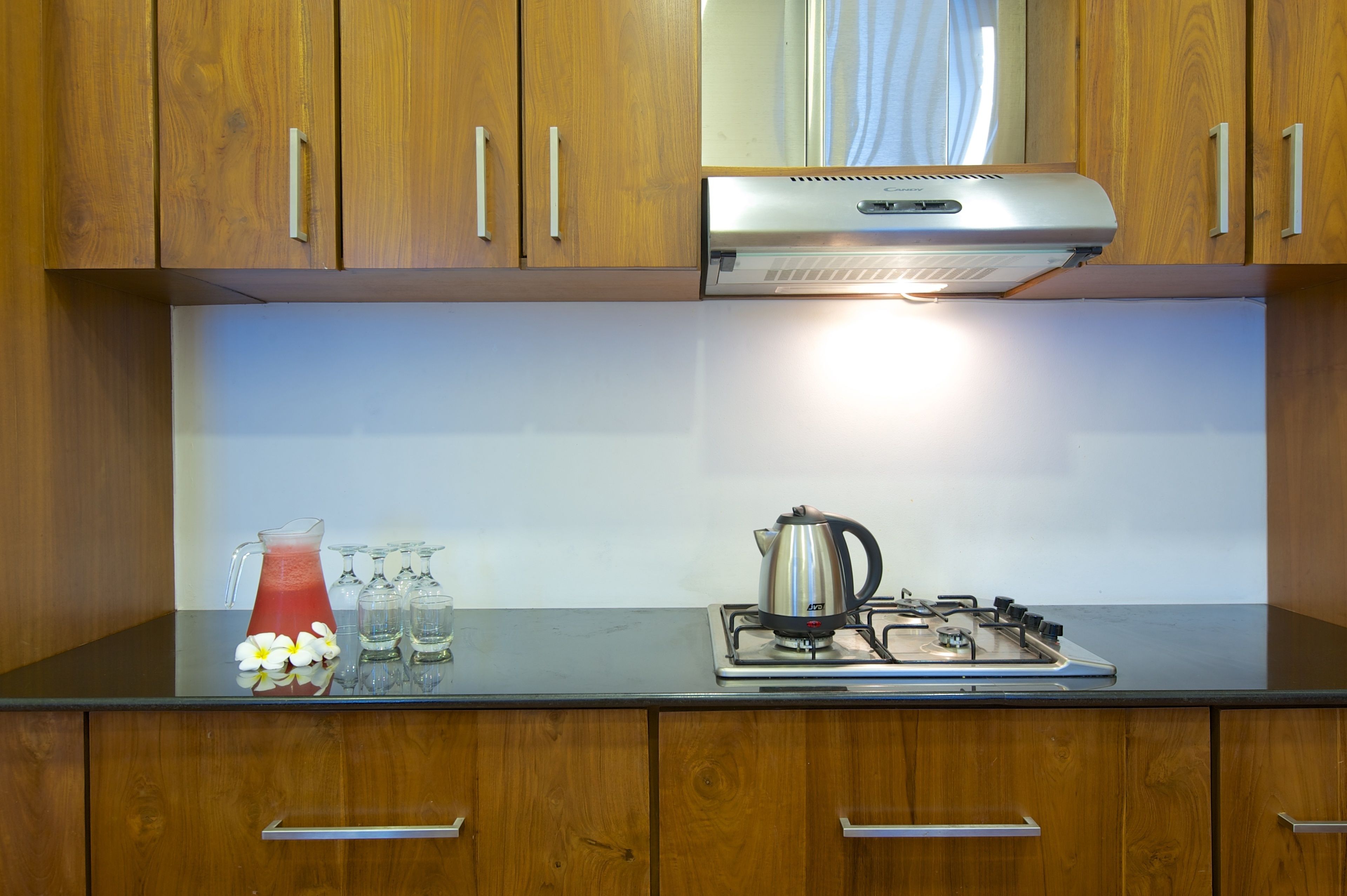 A kitchen with wooden cabinets, a stainless steel range hood, a kettle, and a pitcher of red drink on the counter.