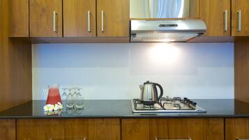 A kitchen with wooden cabinets, a stainless steel range hood, a kettle, and a pitcher of red drink on the counter.