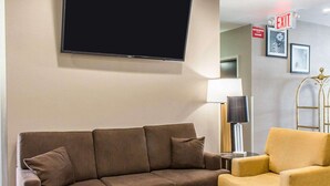 A living room with a brown sofa, a yellow armchair, a round coffee table, a flat-screen TV mounted on the wall, a floor lamp, and an exit sign. - Sleep Inn Coney Island (Brooklyn)