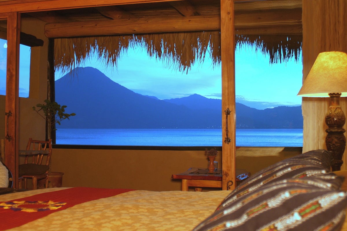 A room with a bed, a TV screen displaying a mountain view, and a wooden ceiling.