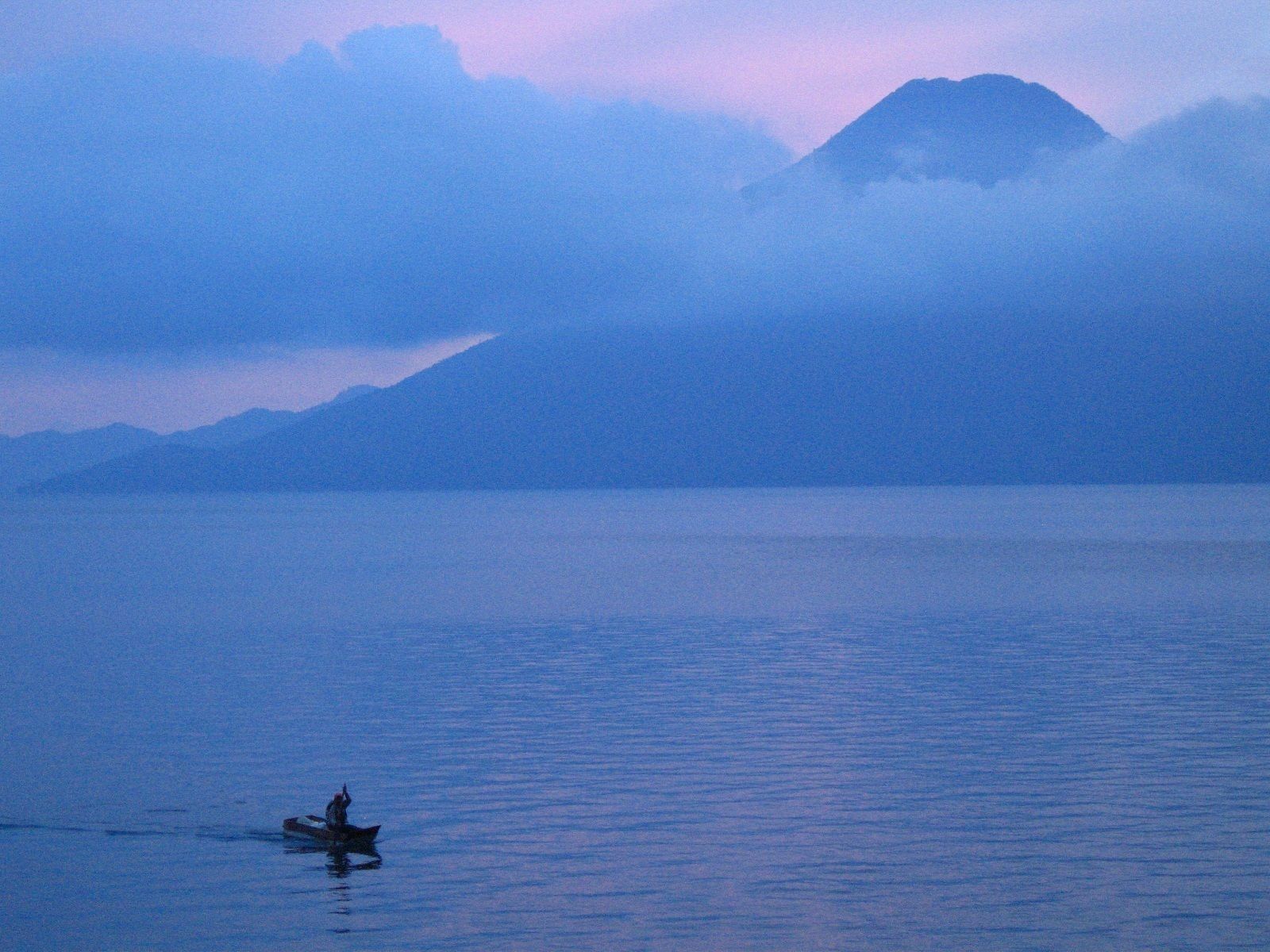A calm body of water with a single boat and a mountain in the background.