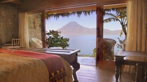 Un dormitorio con una cama grande, una mesa de madera y vista a un cuerpo de agua y una montaña.