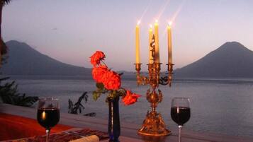 Una mesa con un candelabro, dos copas de vino tinto y un jarrón con flores rojas.