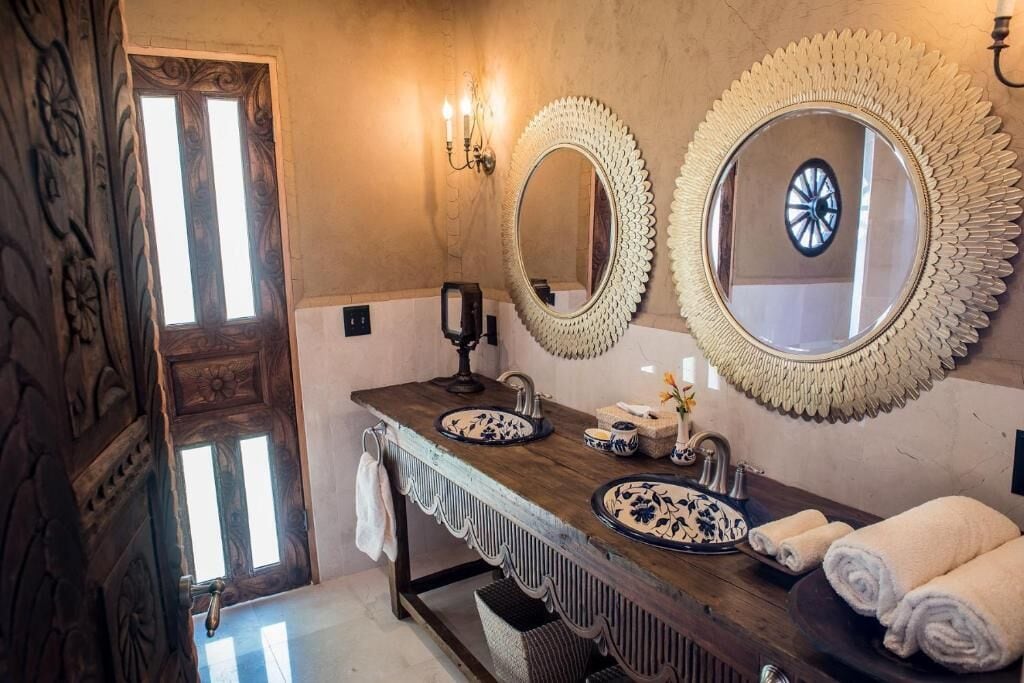 Un baño con tocador de madera, dos espejos, un lavamanos y un perchero para toallas.