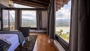 Una camera da letto con un'ampia finestra, un letto, una sedia e vista su un lago e montagne.
