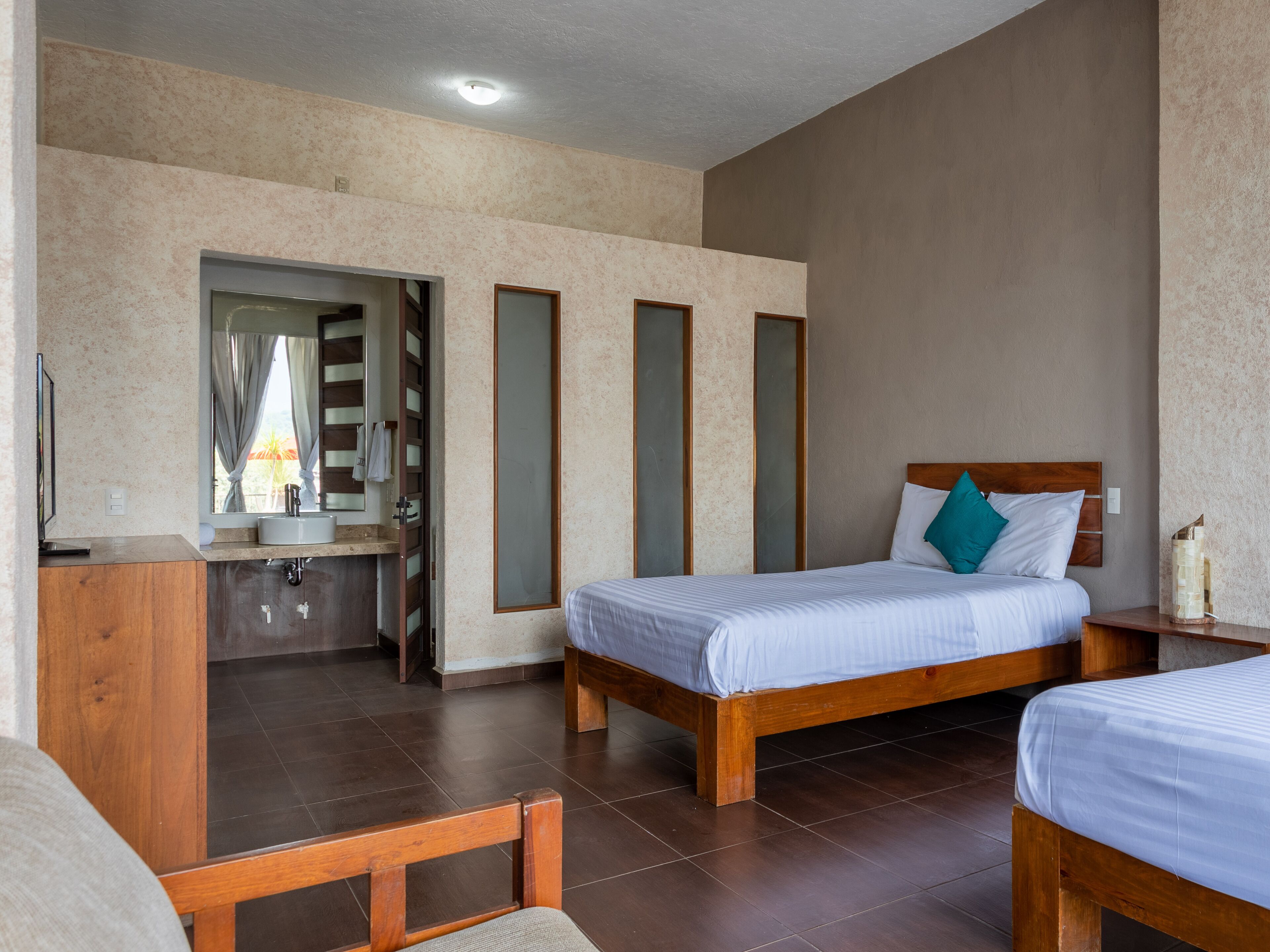 A hotel room with two wooden beds, a bathroom with a mirror, and a view of the outside.