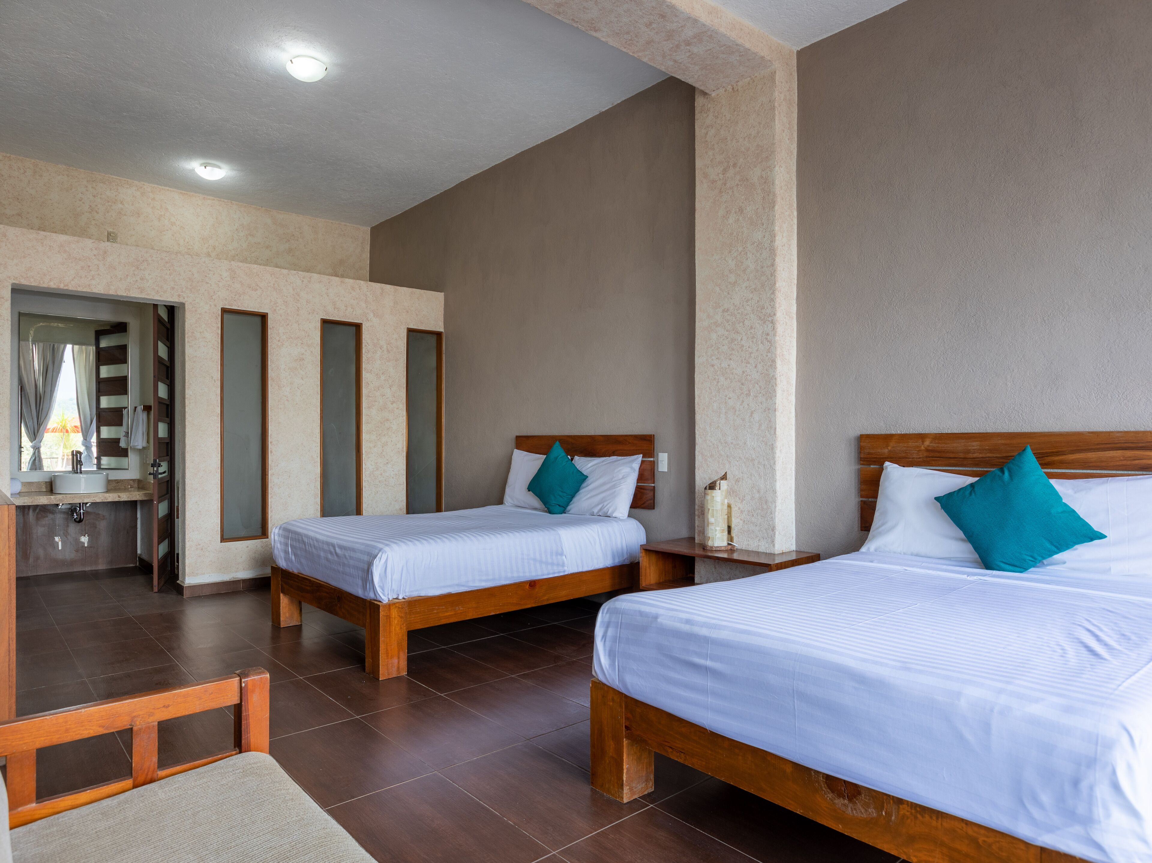 Una habitación de hotel con dos camas de madera, un baño con lavamanos y un espejo.