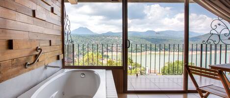 A bathroom with a large bathtub, wooden wall paneling, and a view of a mountainous landscape through a balcony.