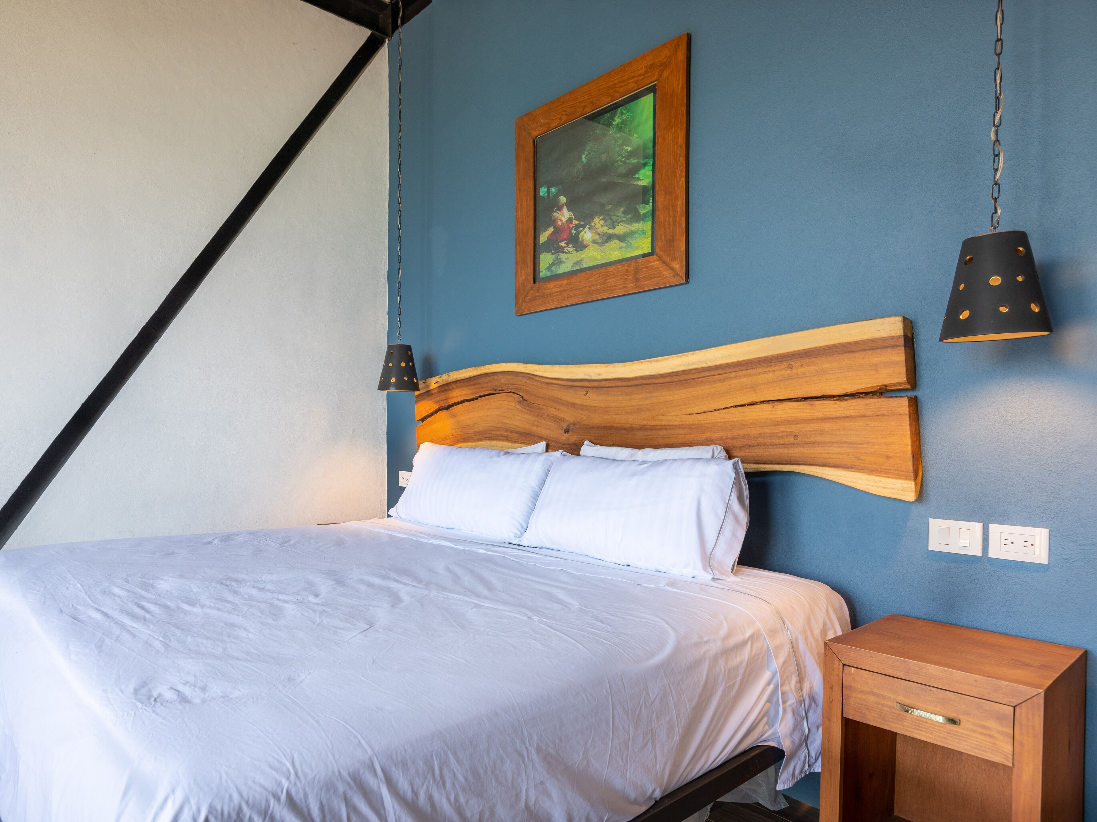 Una cama con cabecera de madera, una mesita de noche y una lámpara colgante.