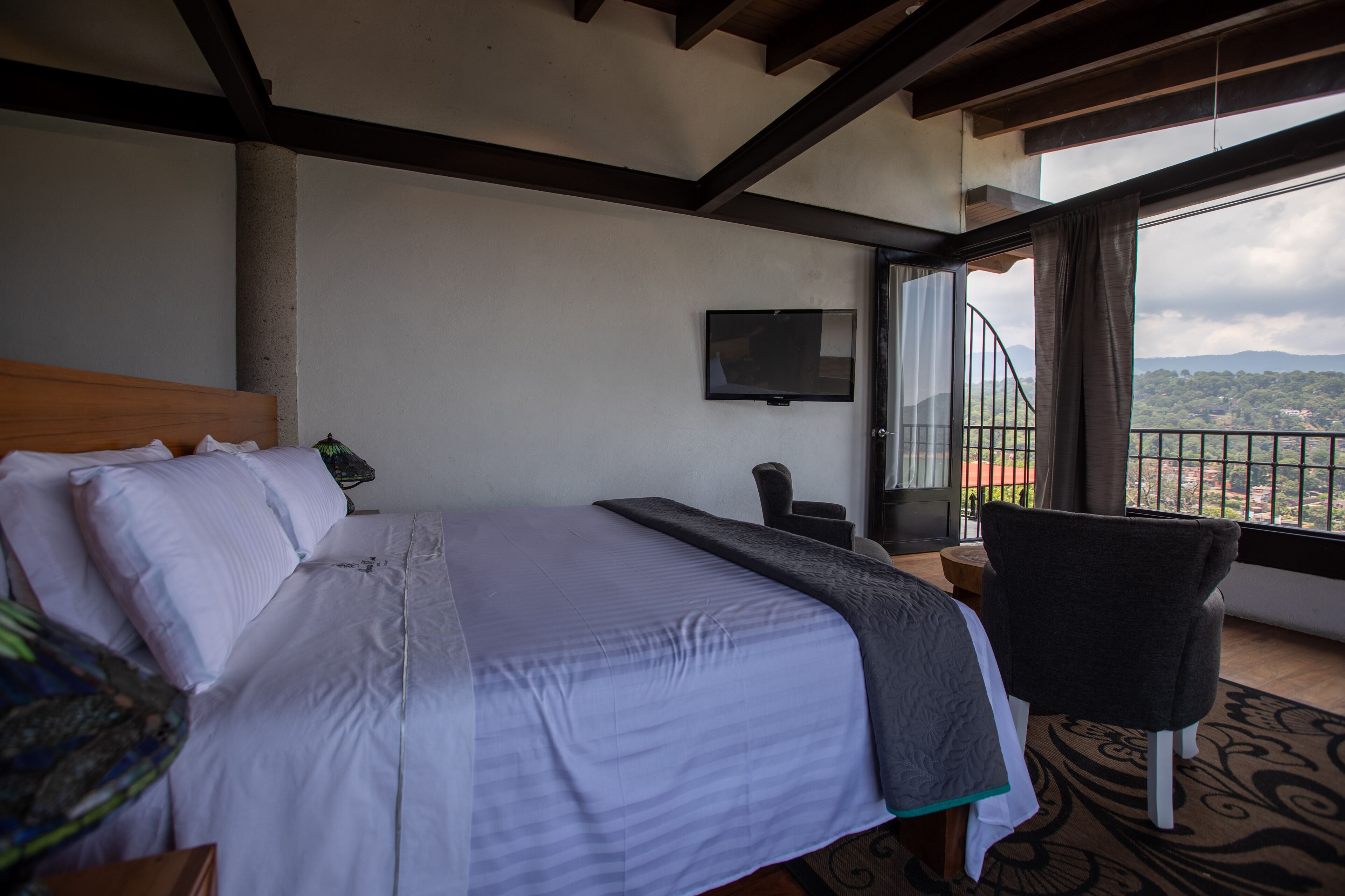 Un dormitorio con cama, una silla, televisor y balcón con vistas al paisaje.