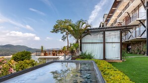 Un hotel moderno con piscina sul tetto, vegetazione lussureggiante e vista sulle montagne lontane.