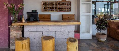 Un mostrador de recepción con encimera de madera, un reloj y un zapatero. Hay tres taburetes de madera frente al mostrador.