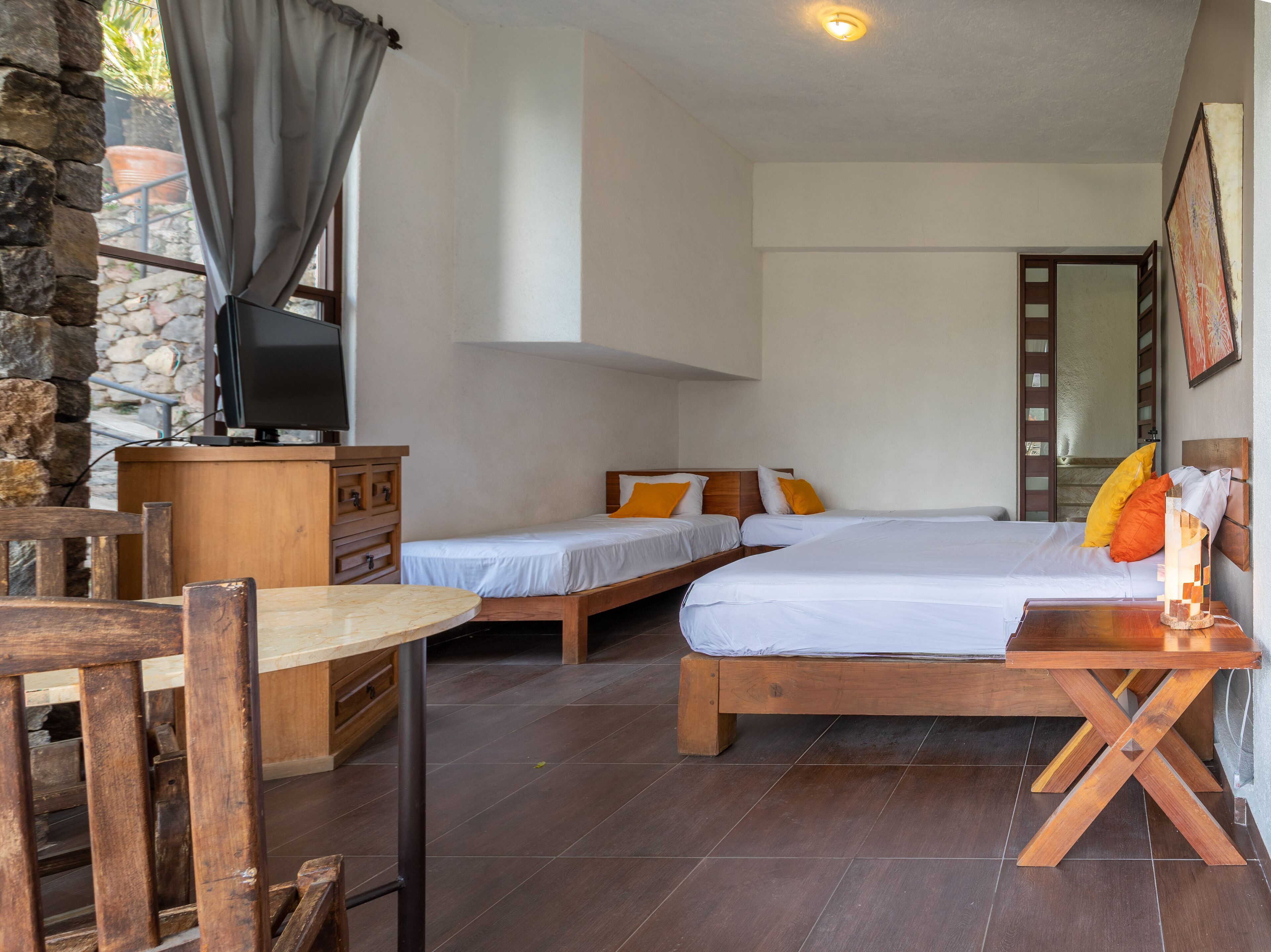 Une chambre avec deux lits simples, un bureau en bois, un téléviseur posé sur une commode et un mur en pierre.