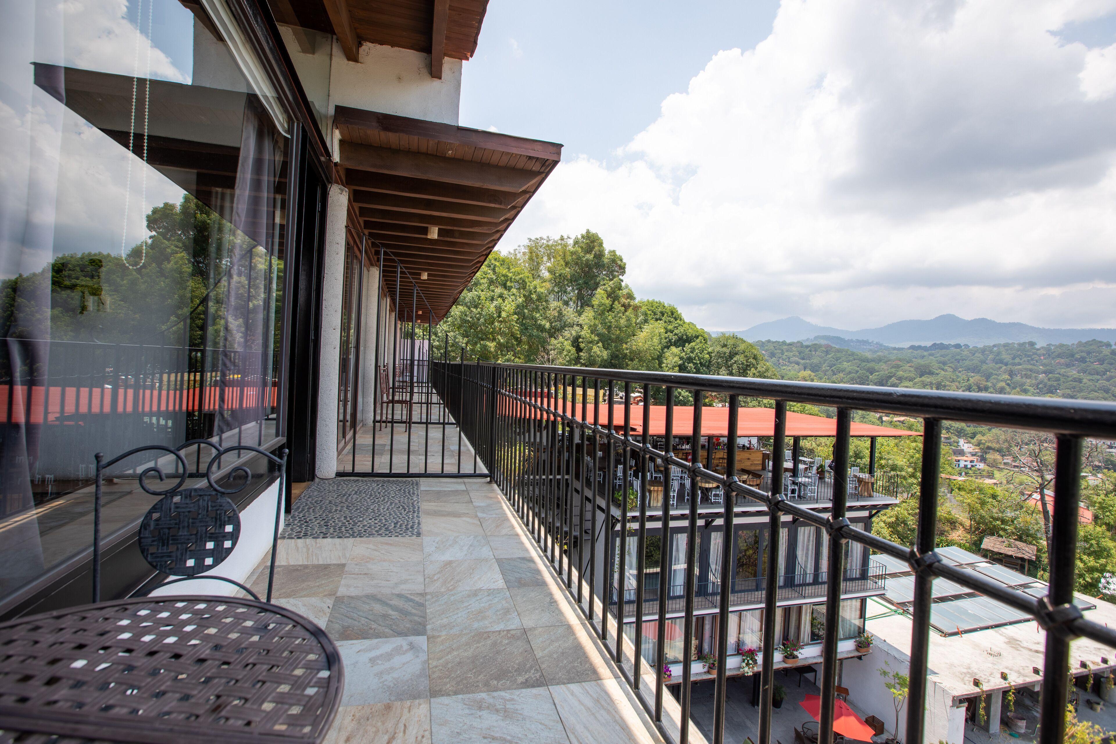 Un balcón con vista a un paisaje montañoso, suelo de baldosas y barandilla de metal.