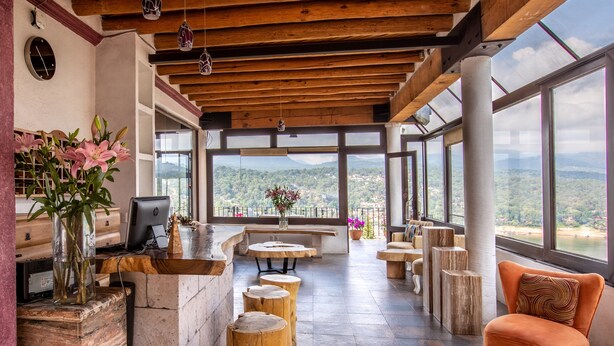 Un'ampia zona relax con soffitto in legno, ampie finestre che offrono vista sul paesaggio e un angolo salotto con tavolino e poltrone.