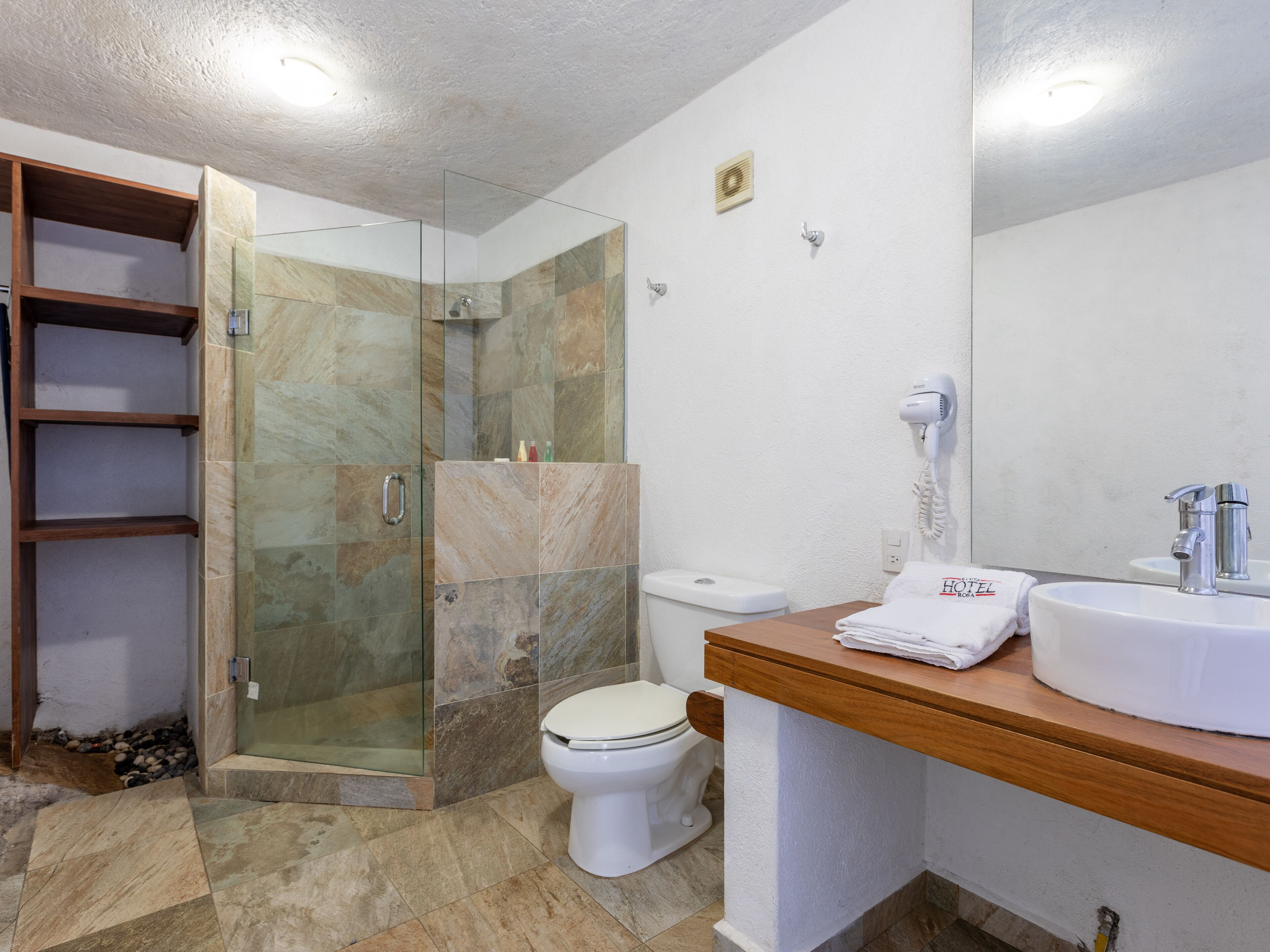 Un baño moderno con ducha envuelta en vidrio, inodoro blanco y lavabo con encimera de madera.