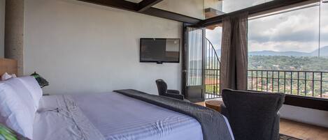 A hotel room with a bed, a TV, a chair, and a balcony with a view of the landscape.
