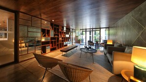 A modern living room with a wooden ceiling, a large bookshelf, a sofa, a coffee table, and a wicker chair. - Lux Lisboa Park (Lisbon)