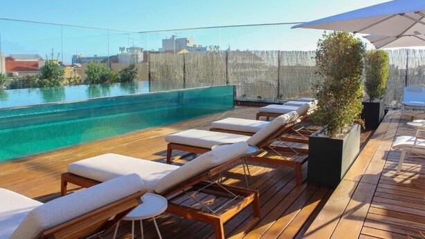 A rooftop pool area with wooden deck, lounge chairs, and a large umbrella. - Lux Lisboa Park (Lisbon)