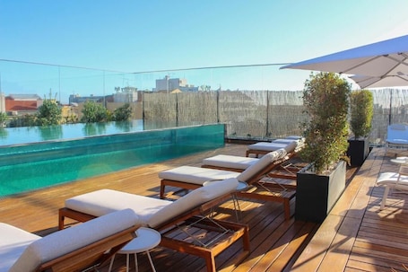 A rooftop pool area with wooden deck, lounge chairs, and a large umbrella.