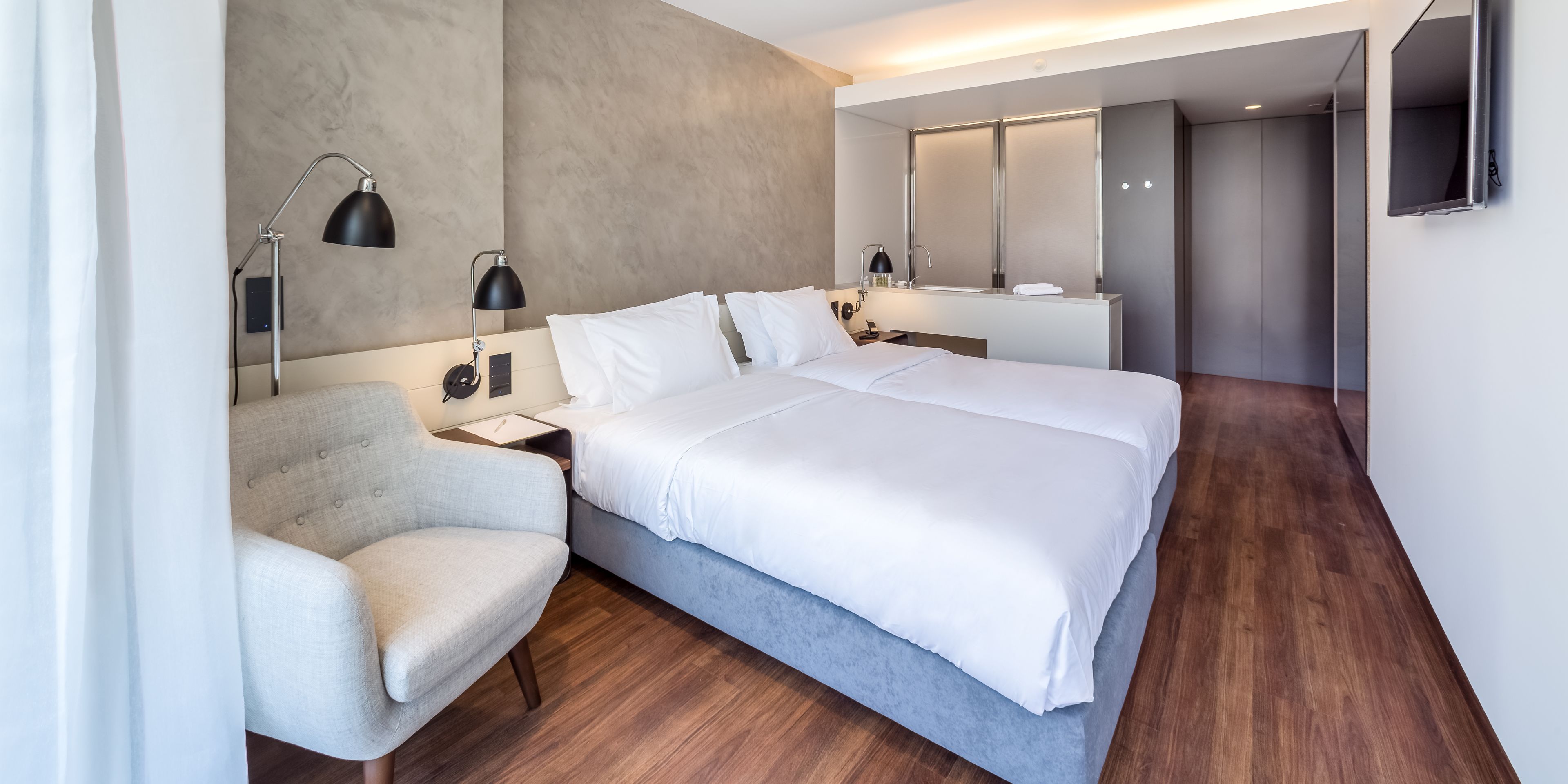 A modern hotel room with a large bed, a chair, a desk, and a mirror.