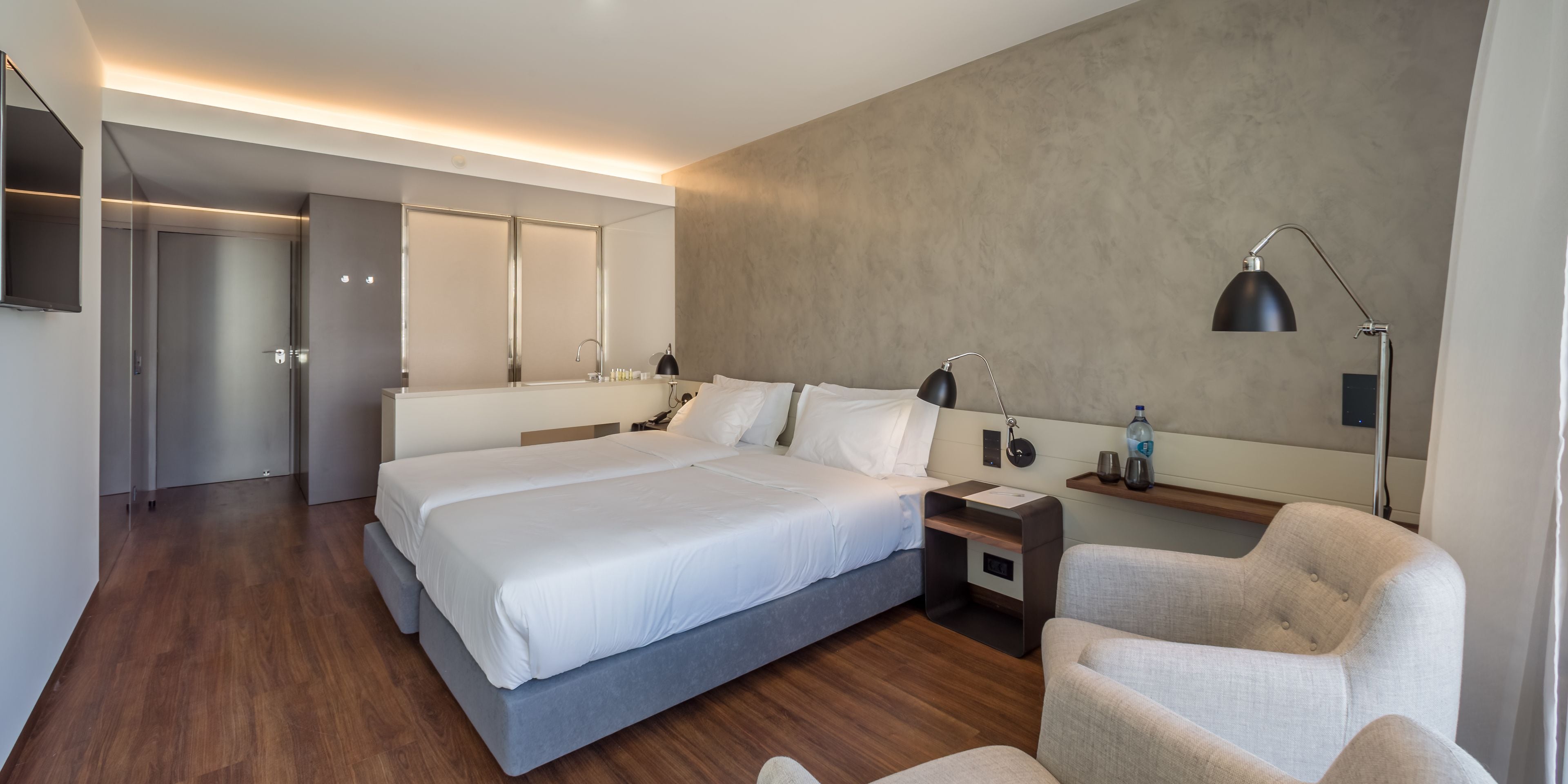 A modern hotel room with a large bed, bedside tables, a chair, and a desk.