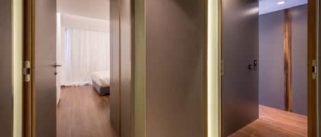 A hotel room with a bed, a wooden floor, and a door leading to another room.