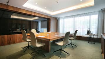 A conference room with a large wooden table, four chairs, and a small side table with a lamp.