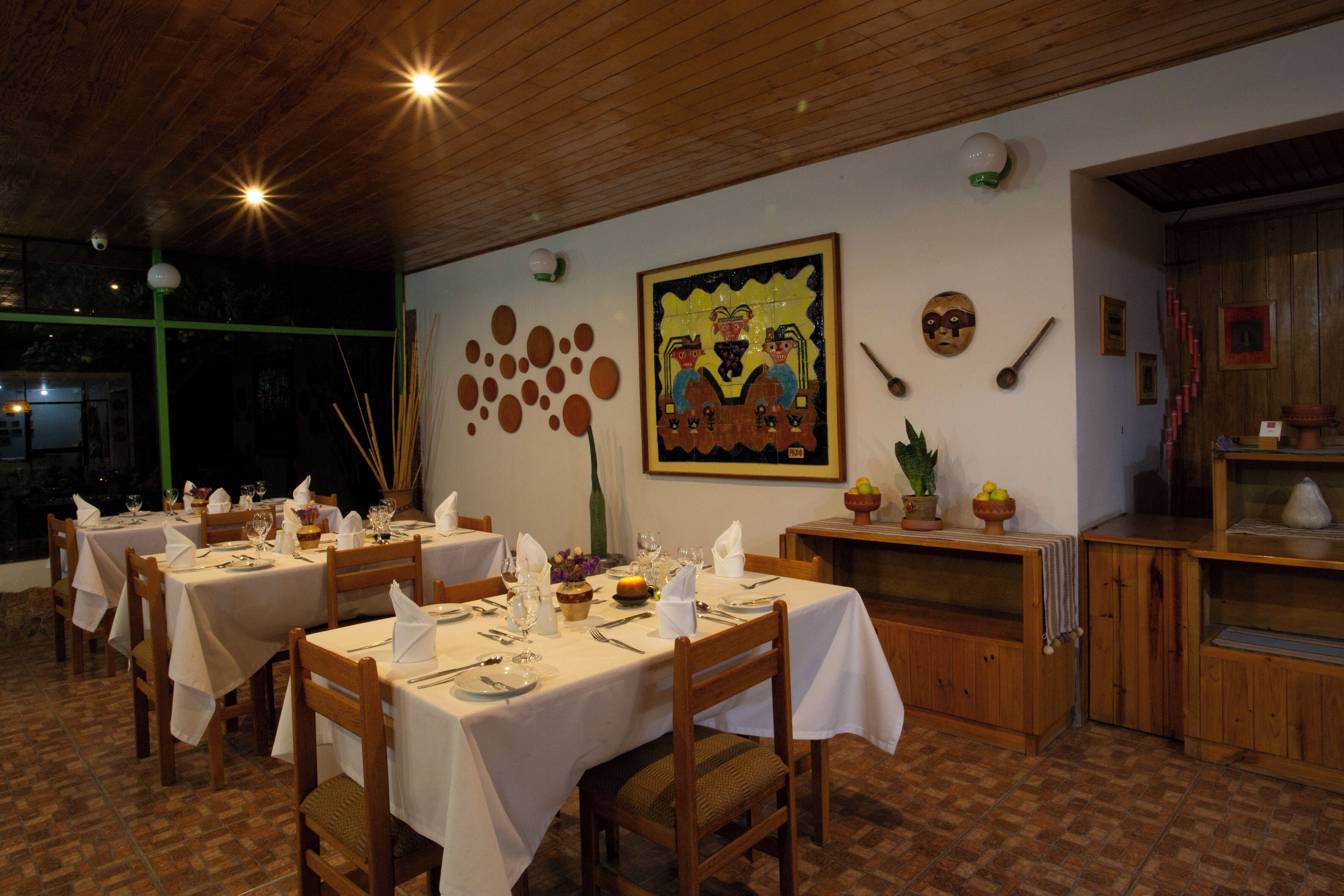Un restaurant avec des tables et des chaises en bois, des nappes blanches et diverses décorations murales, notamment un tableau encadré et des masques.