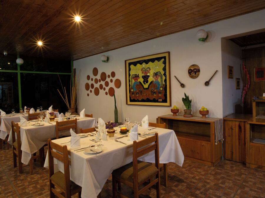Un restaurant avec des tables et des chaises en bois, des nappes blanches et diverses décorations murales, notamment un tableau encadré et des masques.